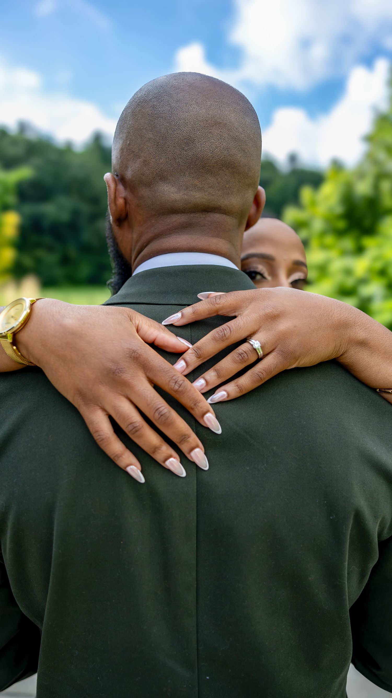 Close-up of hands with wedding rings embracing across formal suit jacket.