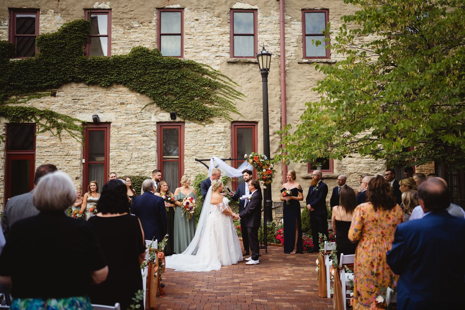 Wedding guests gathered outside a rustic stone building during an outdoor ceremony.