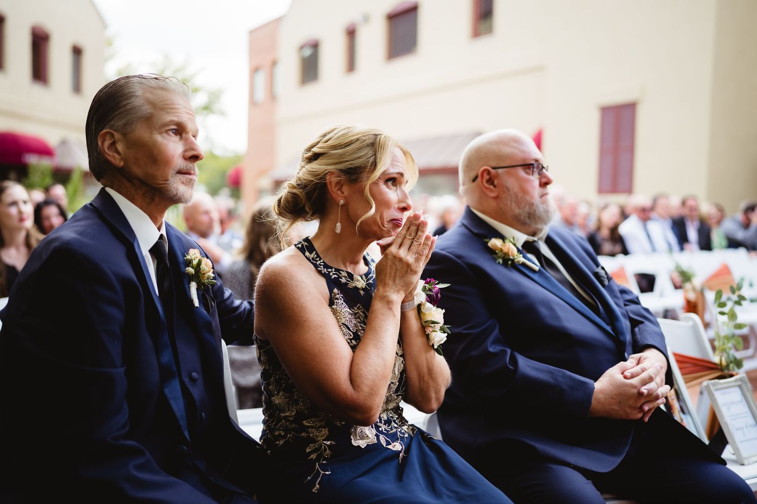 Guests in formal attire sit in rows during a wedding ceremony, reacting emotionally to the proceedings.