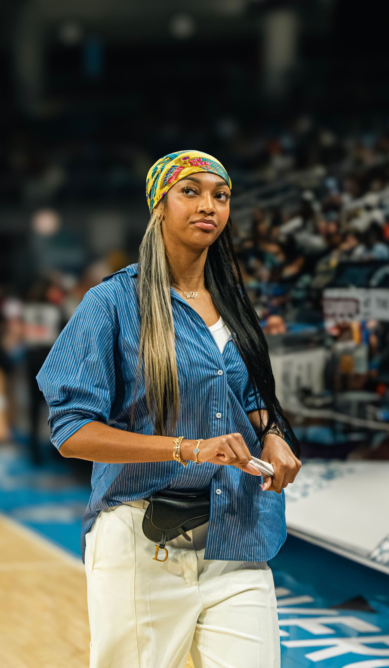 A performer in casual denim and white outfit standing on a basketball court during a sporting event.