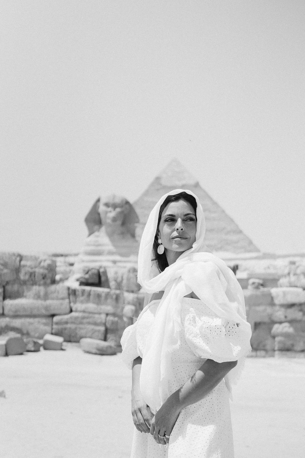 A flowing white dress billows in the wind against the backdrop of ancient Egyptian pyramids in Giza.