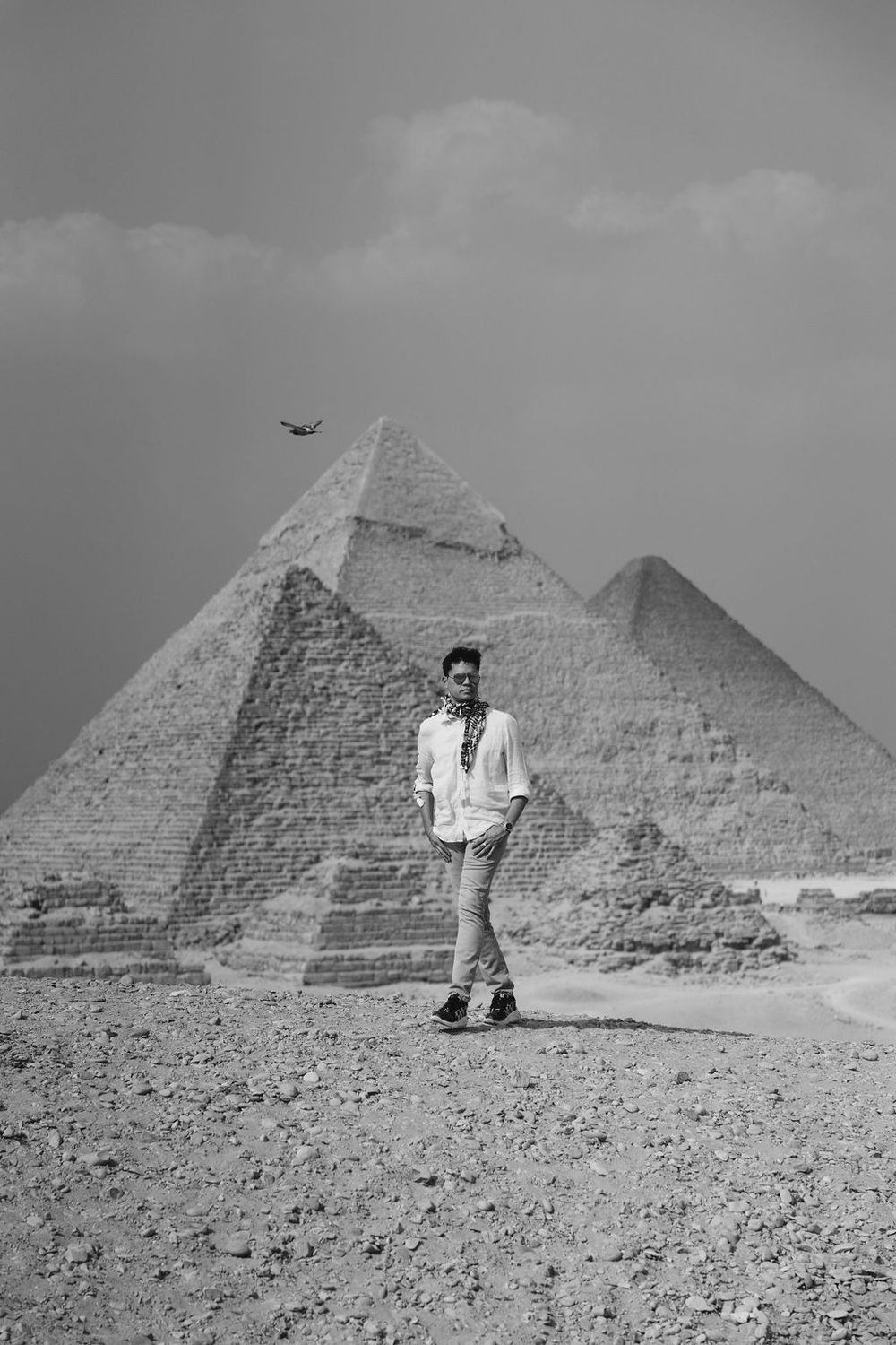 Black and white photograph showing a person standing in front of the iconic pyramids of Giza in Egypt.