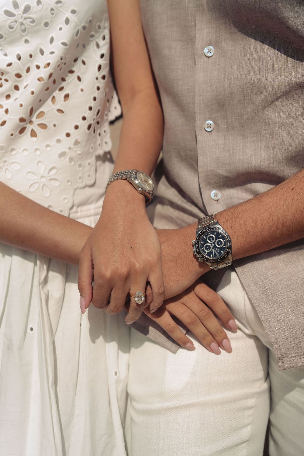 Close-up of hands wearing elegant jewelry showing a silver bracelet, ring and watch against beige and white clothing.