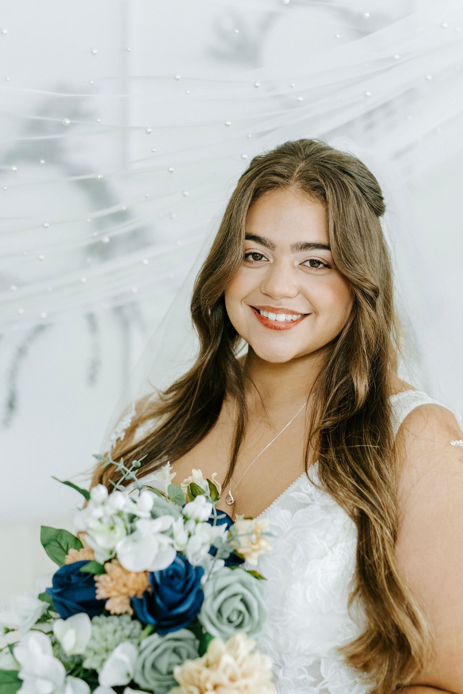 Bridal portrait series with romantic bouquet featuring blue, white and peach flowers against light background.