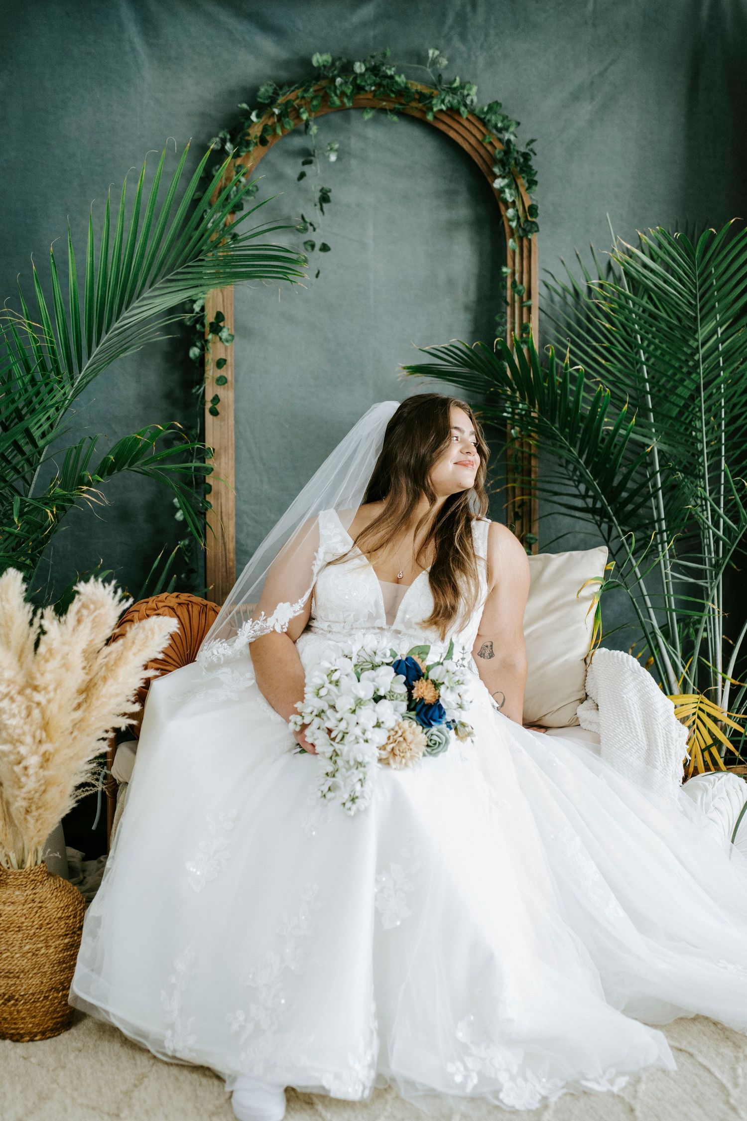 Bridal portraits with white dress against grey backdrop with tropical palms and wooden arch decor.