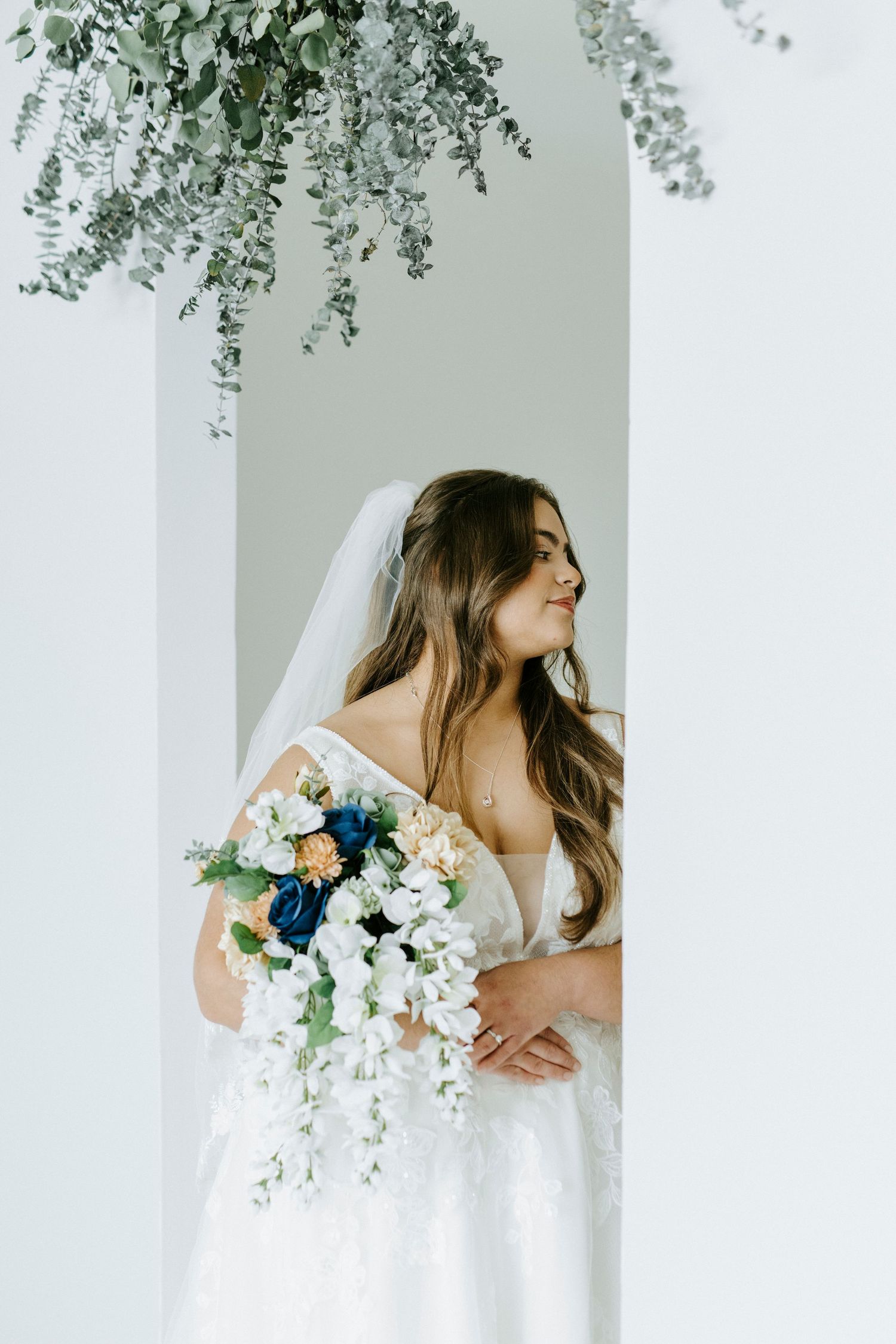 A side profile bridal photo with cascading white flowers and delicate veil against a minimalist backdrop.