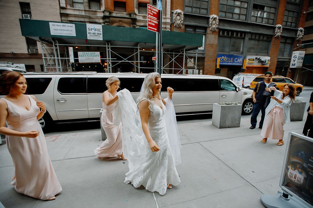 Women in white dresses walking on a city sidewalk outside a historic theater building.