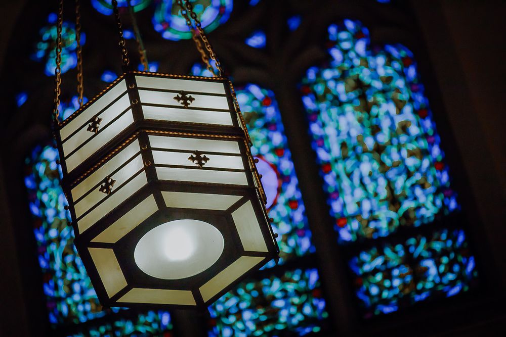 Elegant lantern light fixtures mounted on wall with stained glass windows in background.