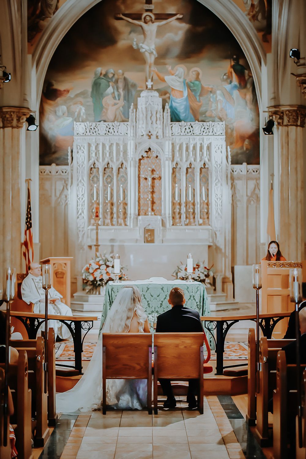 Interior view of a church sanctuary with wooden pews and ornate altar featuring religious artwork and decorations.
