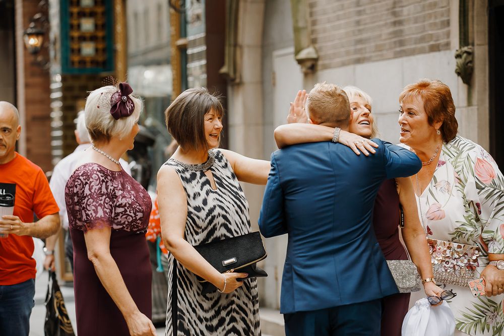 People dancing together in pairs along a stone building wall during a social gathering.
