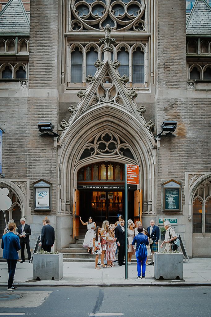 People gathered outside a Gothic-style church entrance with ornate stone architecture and arched doorways.