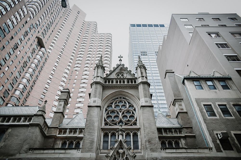 Looking up at historic Gothic church architecture with spires and decorative elements against modern buildings.