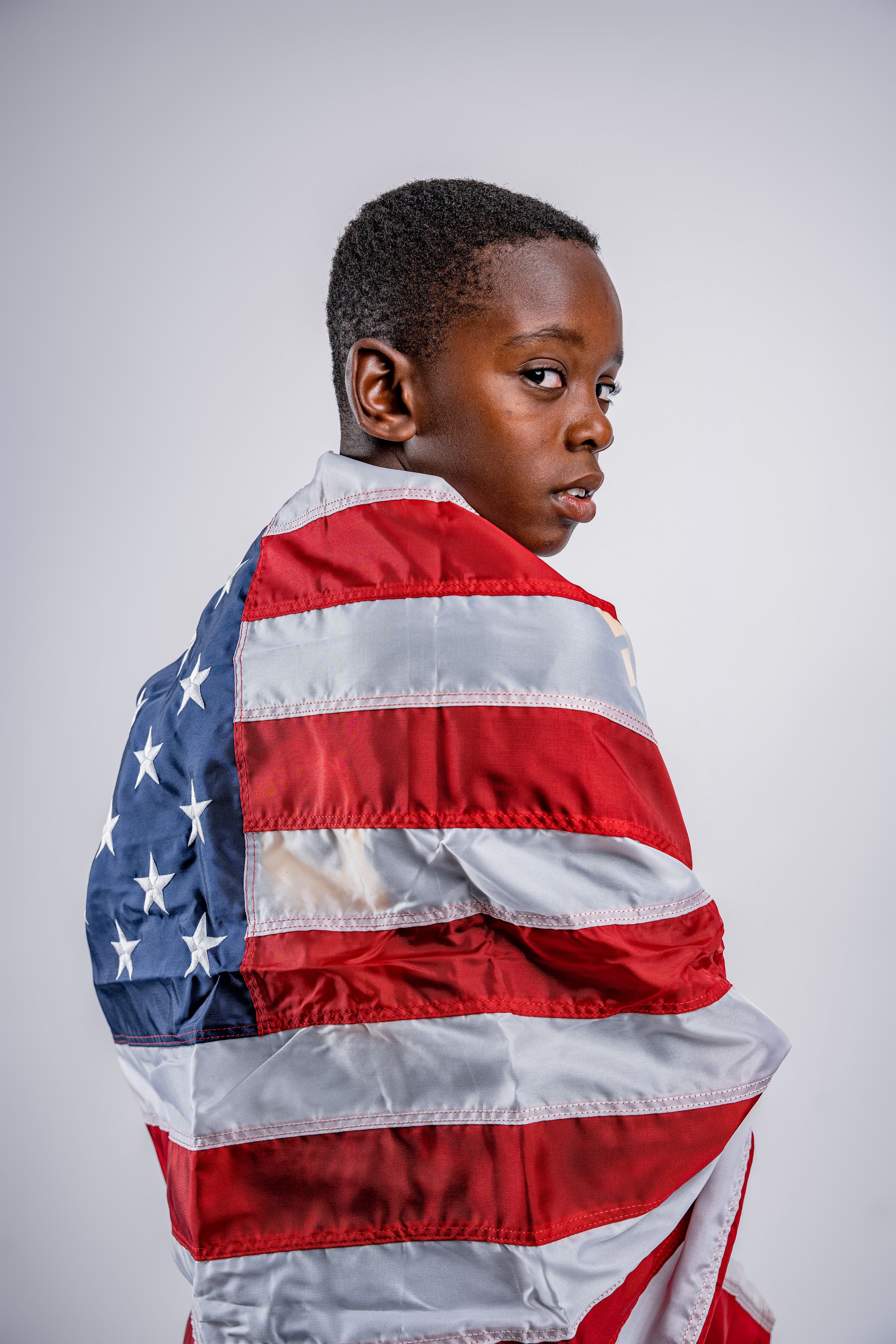 Multiple shots of someone wrapped in an American flag against a light gray background, creating a patriotic portrait series.