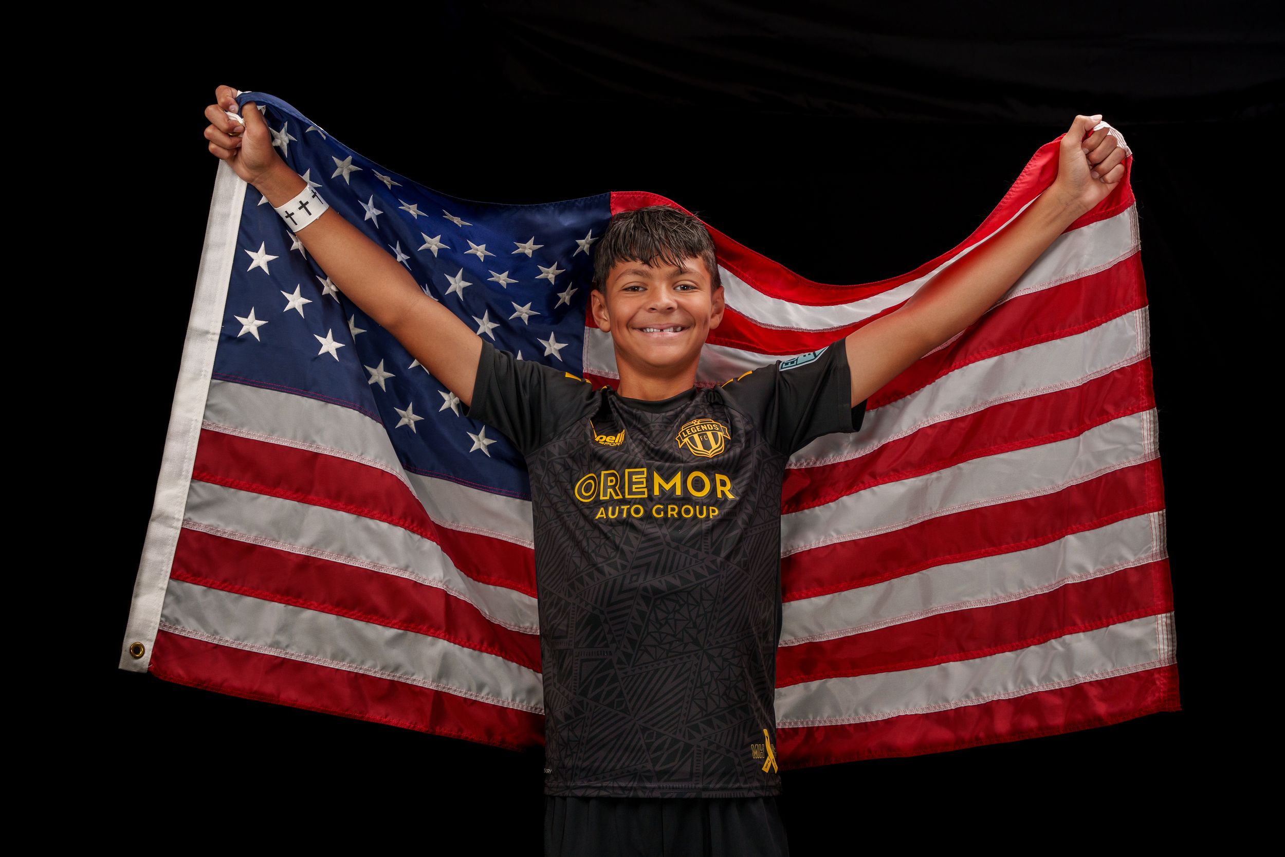 A person stands in front of a black background holding up an American flag in a patriotic display.