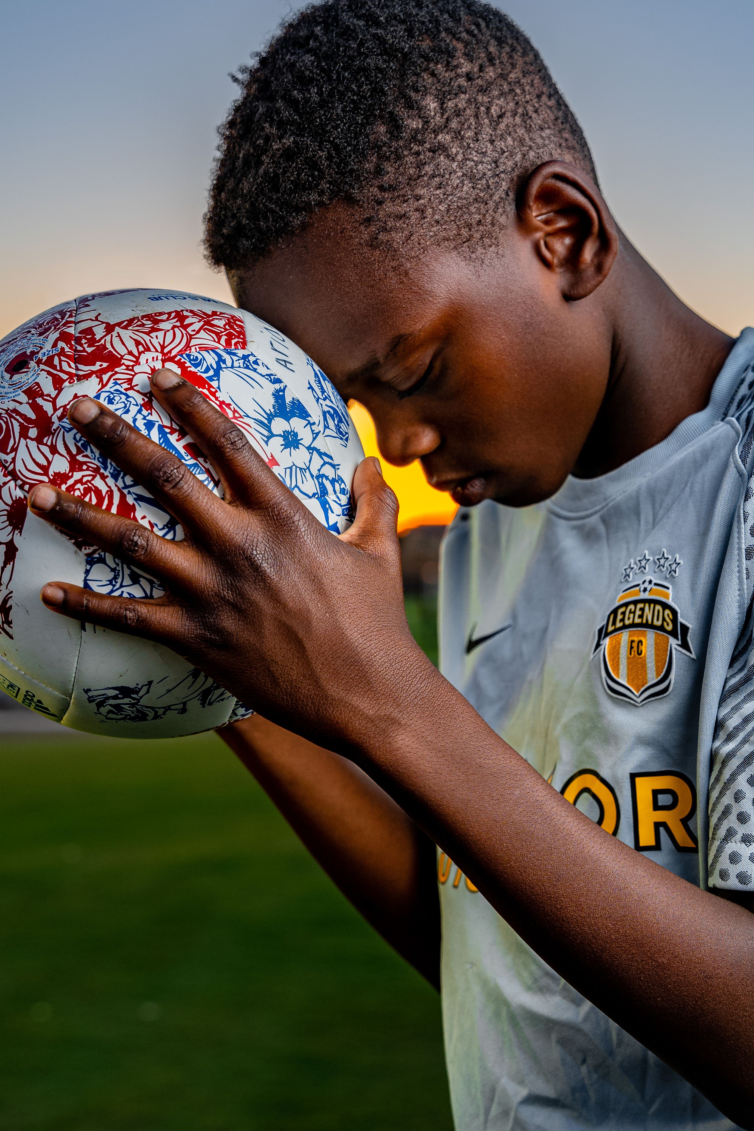 A person wearing a sports jersey bows their head in an outdoor setting at sunset, showing a moment of reflection.