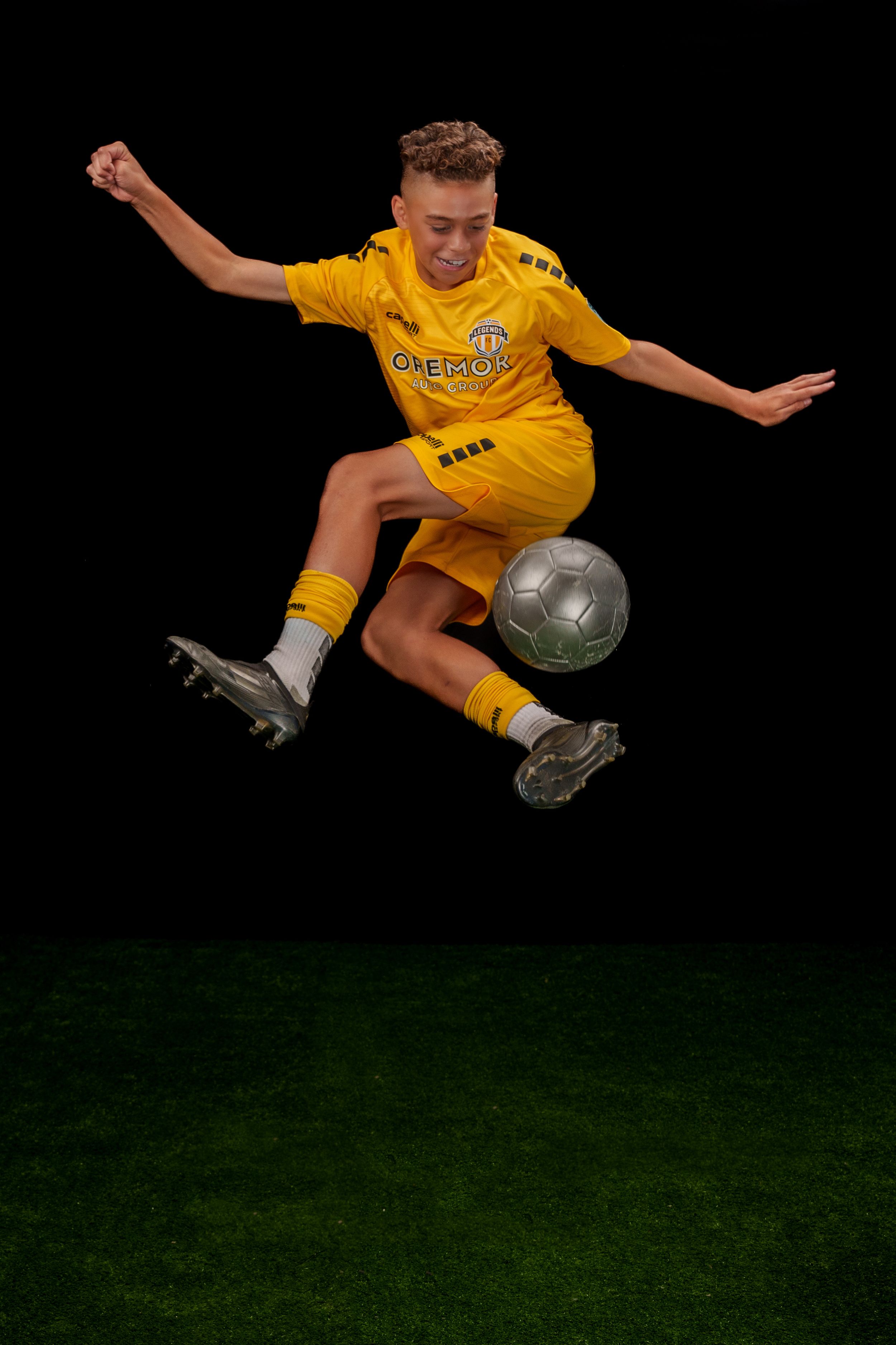Soccer player in yellow jersey performs dramatic flying kick with soccer ball against dark background.