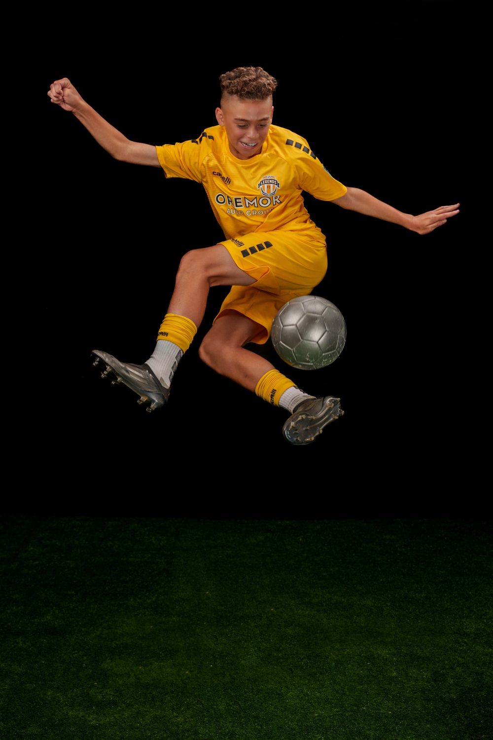 Soccer player in yellow jersey performs dramatic flying kick with soccer ball against dark background.
