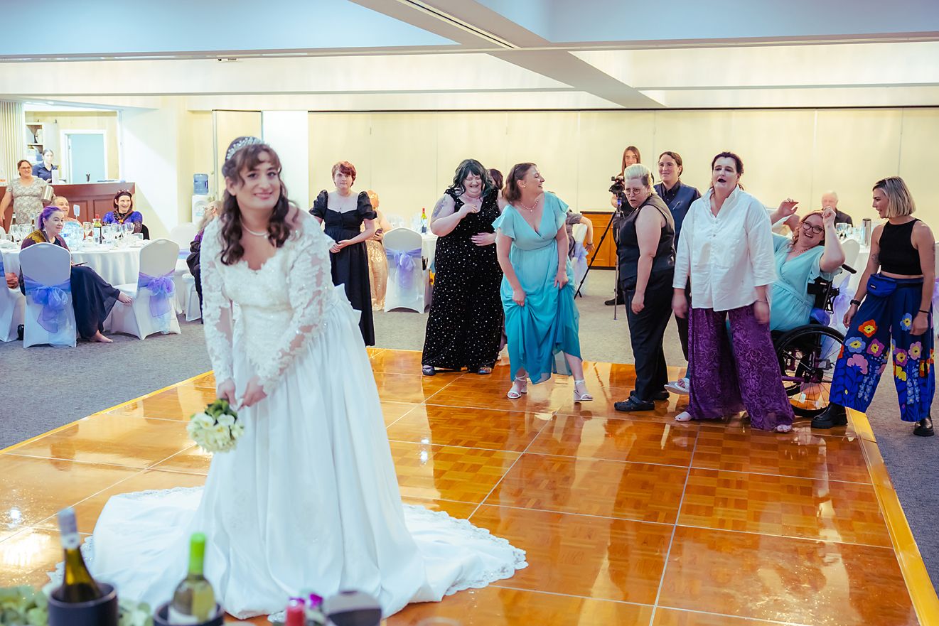 Wedding guests dance together on a polished wooden dance floor at a reception venue.