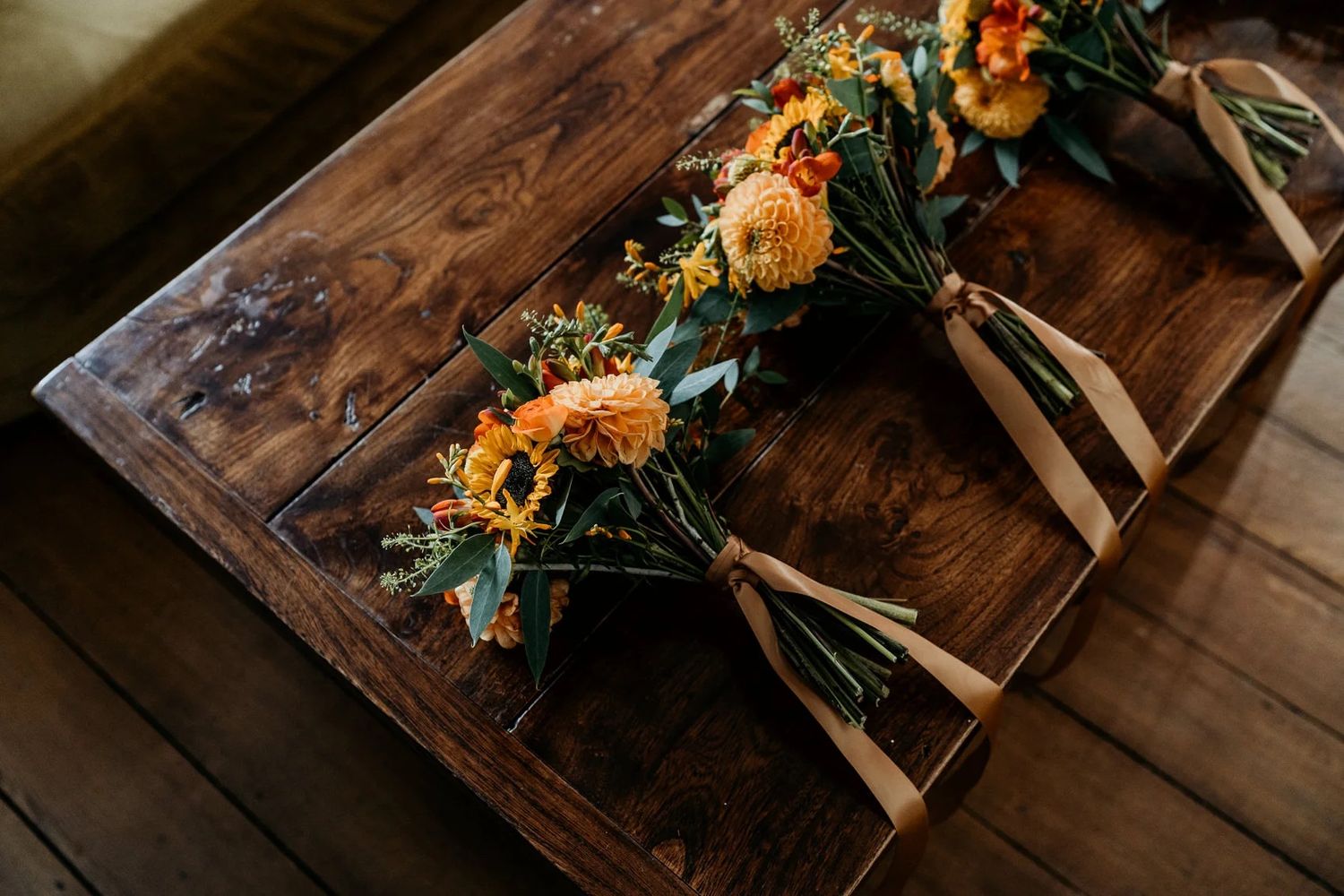 Wedding decor details featuring rustic wooden tables adorned with orange and yellow floral centerpieces.