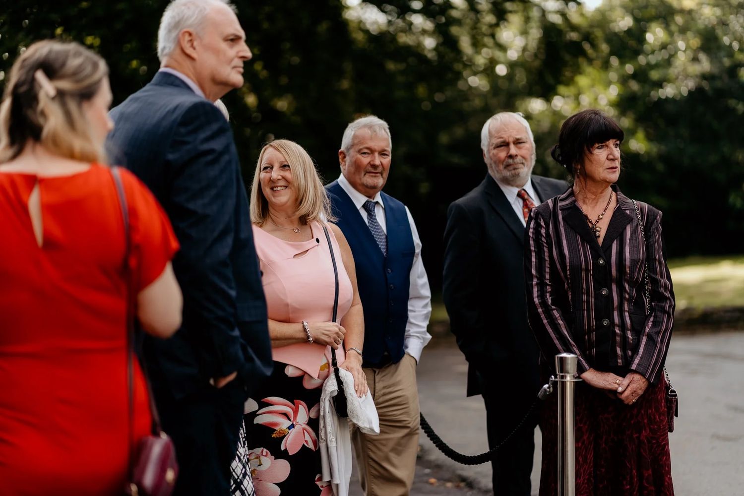 A small group of wedding guests gathered outdoors in formal attire chatting before the ceremony.