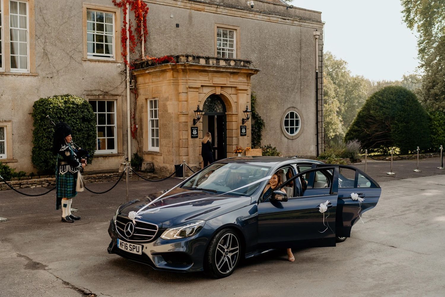 A sleek black Mercedes-Benz parked outside an elegant stone mansion entrance.