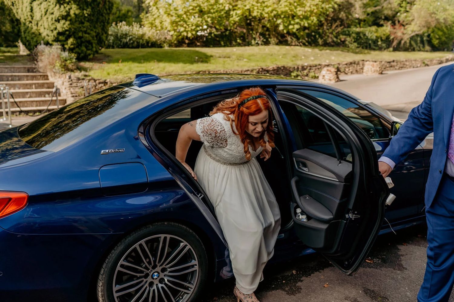 Wedding party arriving in luxury cars with navy blue vehicle in golden afternoon sunlight.