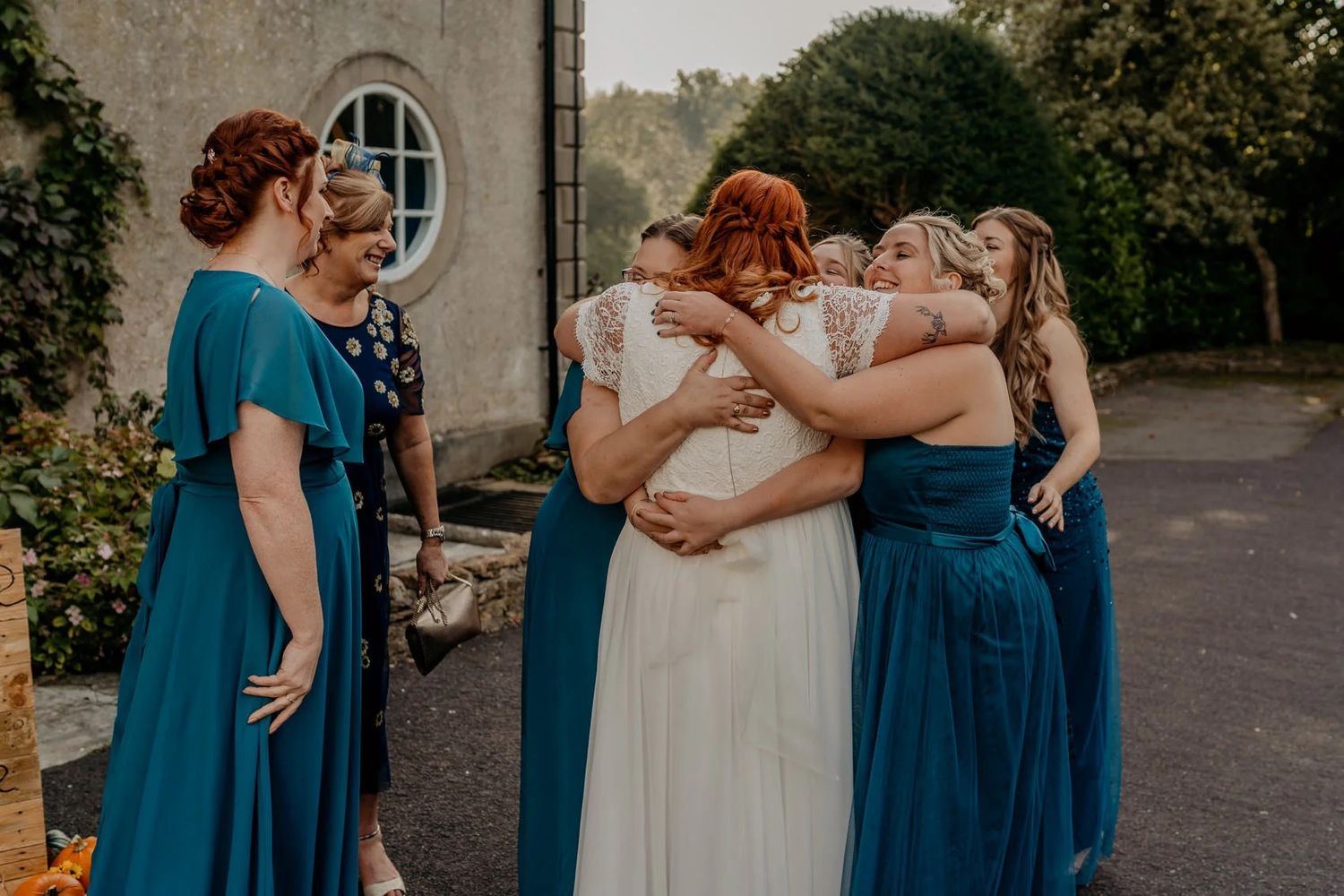 Bridesmaids in blue dresses share an emotional group hug during wedding celebrations.