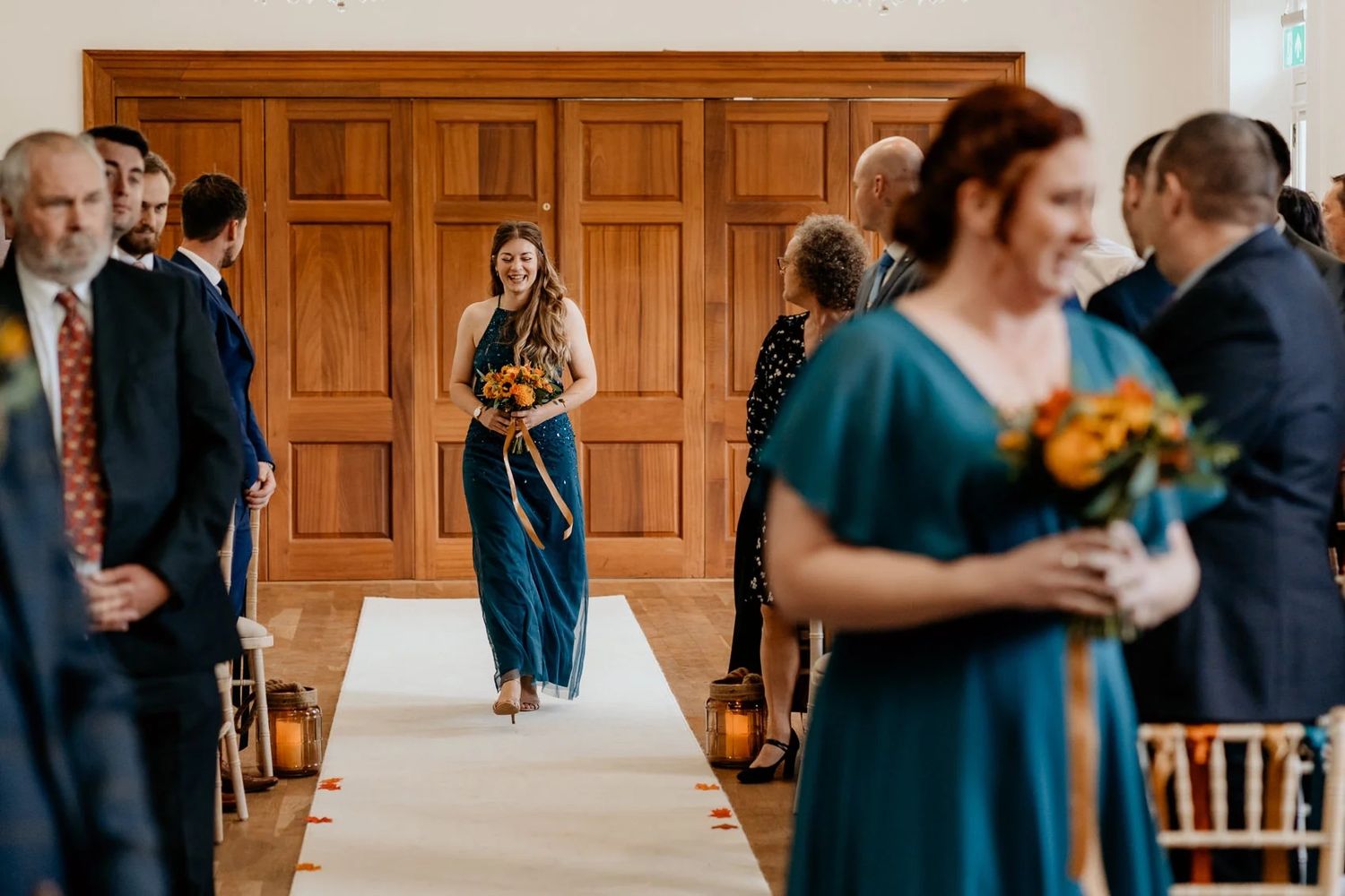 Wedding guests mingle and dance in an elegant wood-paneled reception hall decorated with hanging lights.