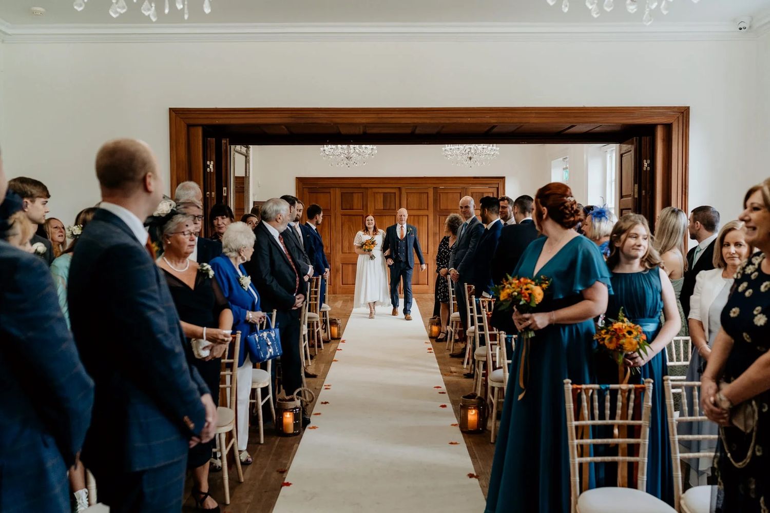 Guests mingle in an elegant reception hall with large wooden doors and chandelier lighting.
