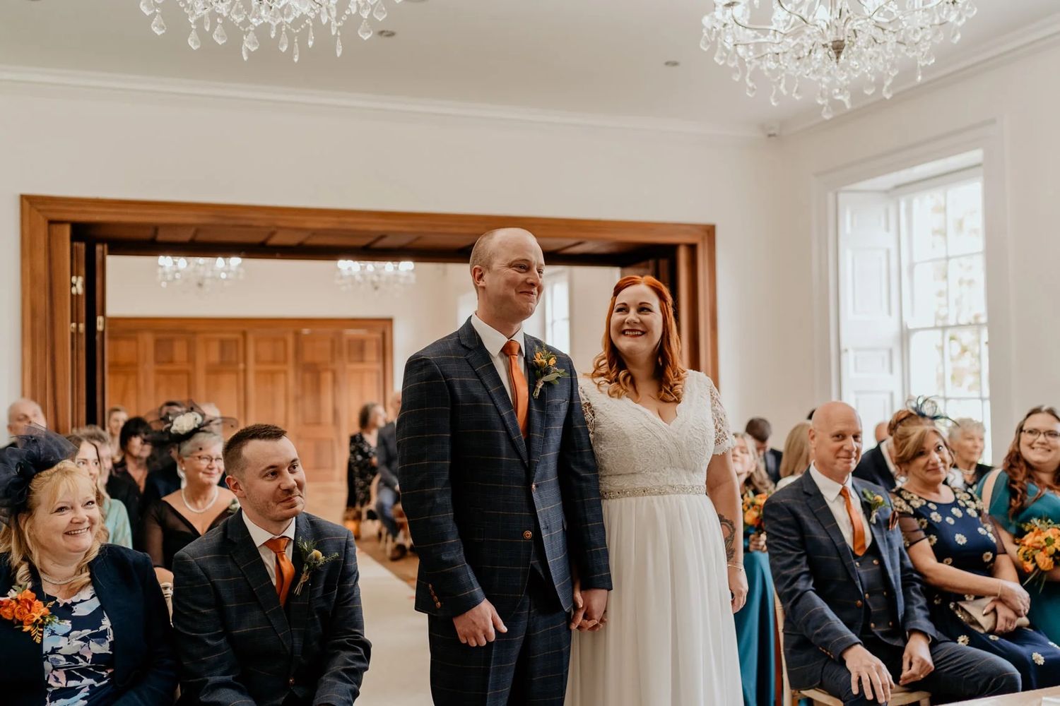Elegant indoor wedding ceremony with guests seated beneath crystal chandeliers.