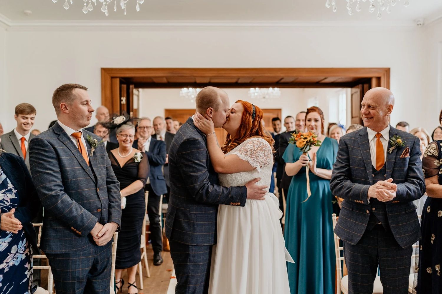 Wedding guests applaud as newlyweds share their first kiss in an elegant indoor venue.