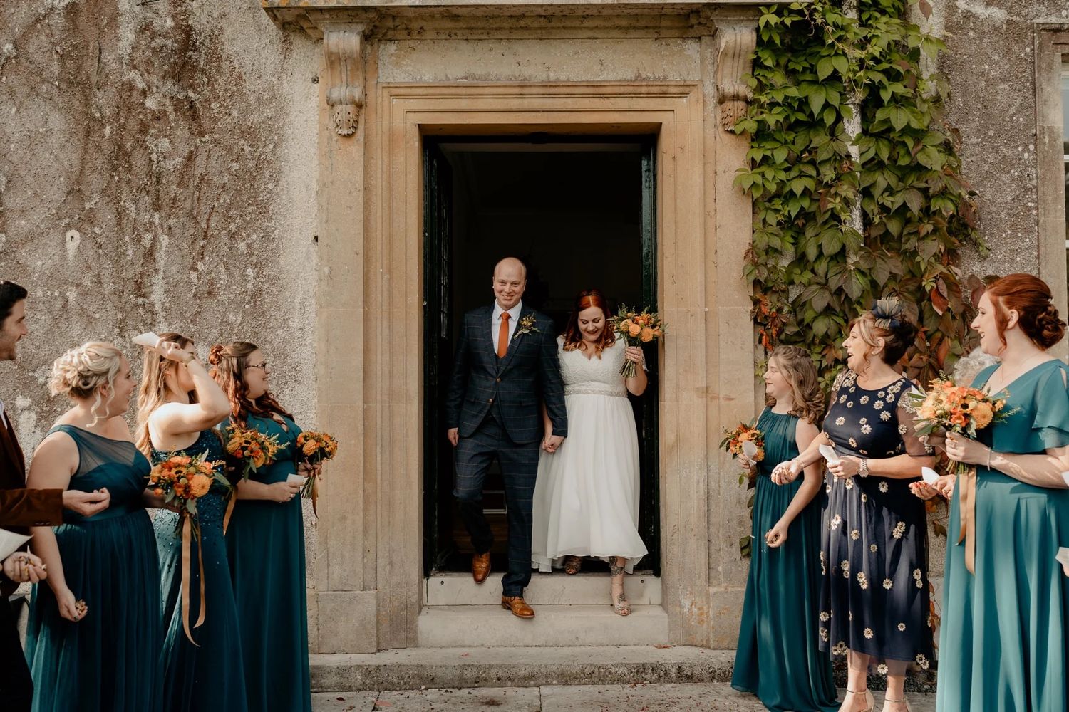 Stone building exterior decorated with ivy serves as backdrop for wedding gathering.