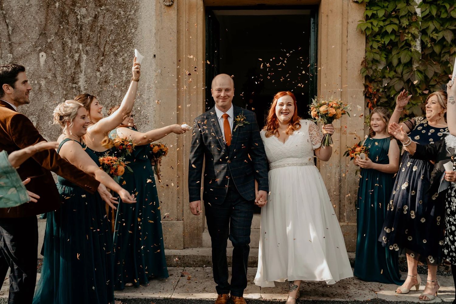 Wedding exit celebration with guests throwing confetti outside stone building entrance.