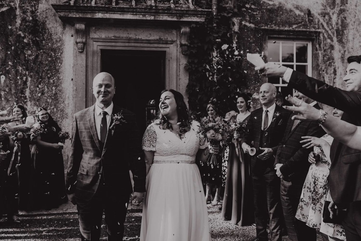 Black and white photo of wedding exit with guests celebrating outside historic building.