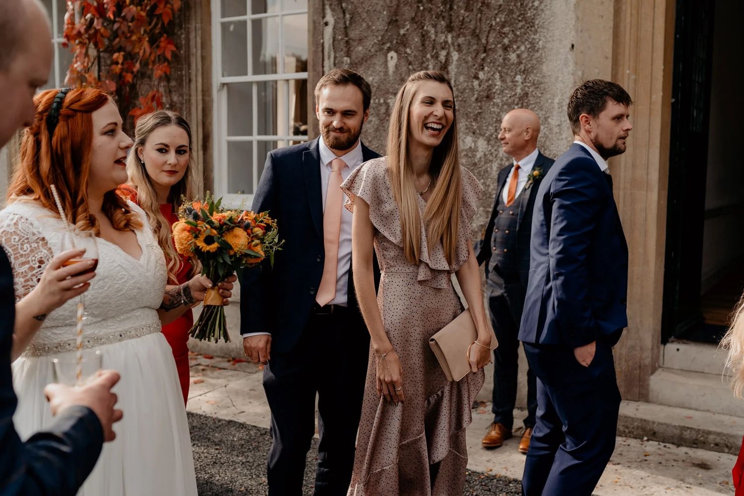 Wedding celebration outside a grand stone mansion with bright fall foliage.