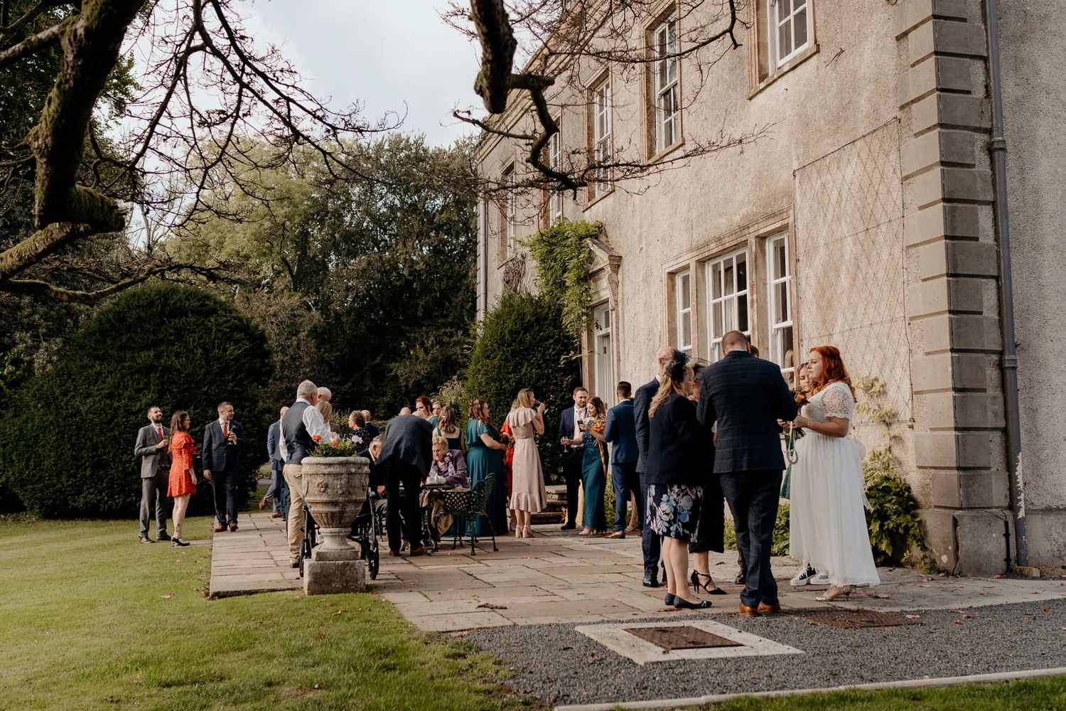 Wedding party gathered outside stately stone building on manicured lawn.