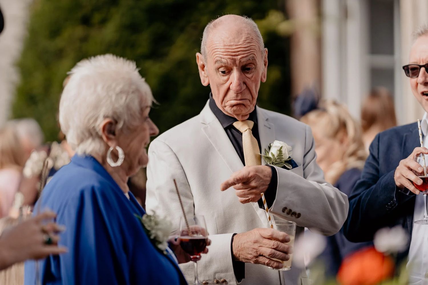 Wedding guests mingling at an outdoor reception wearing formal attire in navy and neutral tones.