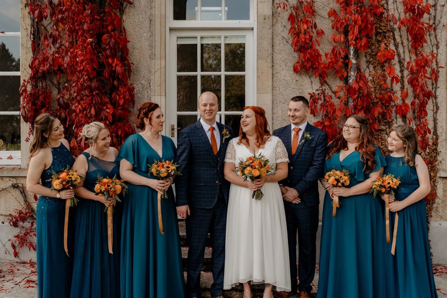 Wedding party in navy blue and white attire poses in front of vine-covered building.