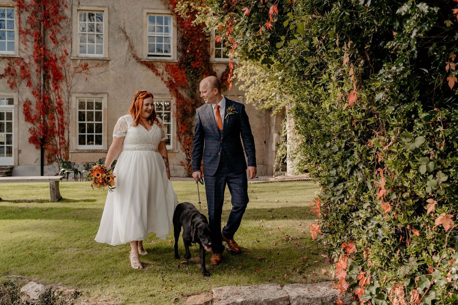 Wedding couple poses in front of historic building with vibrant fall foliage.