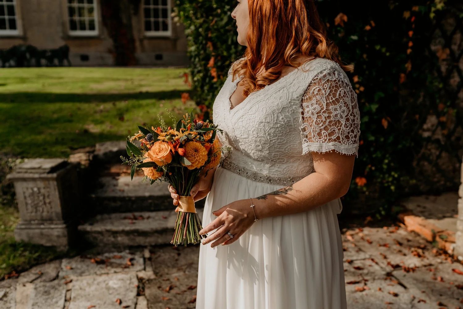 Bride holding autumn bouquet against backdrop of red ivy-covered building.