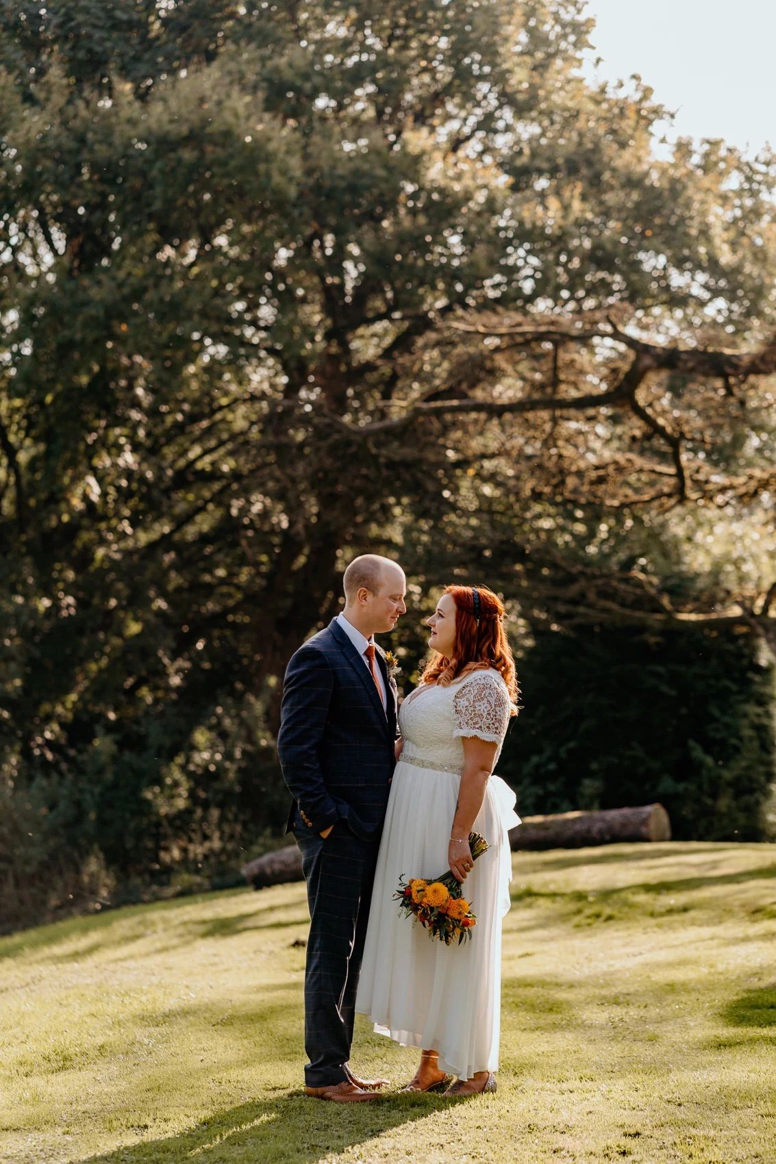 Beautiful outdoor wedding ceremony on grassy hillside with sunlit oak trees in background.