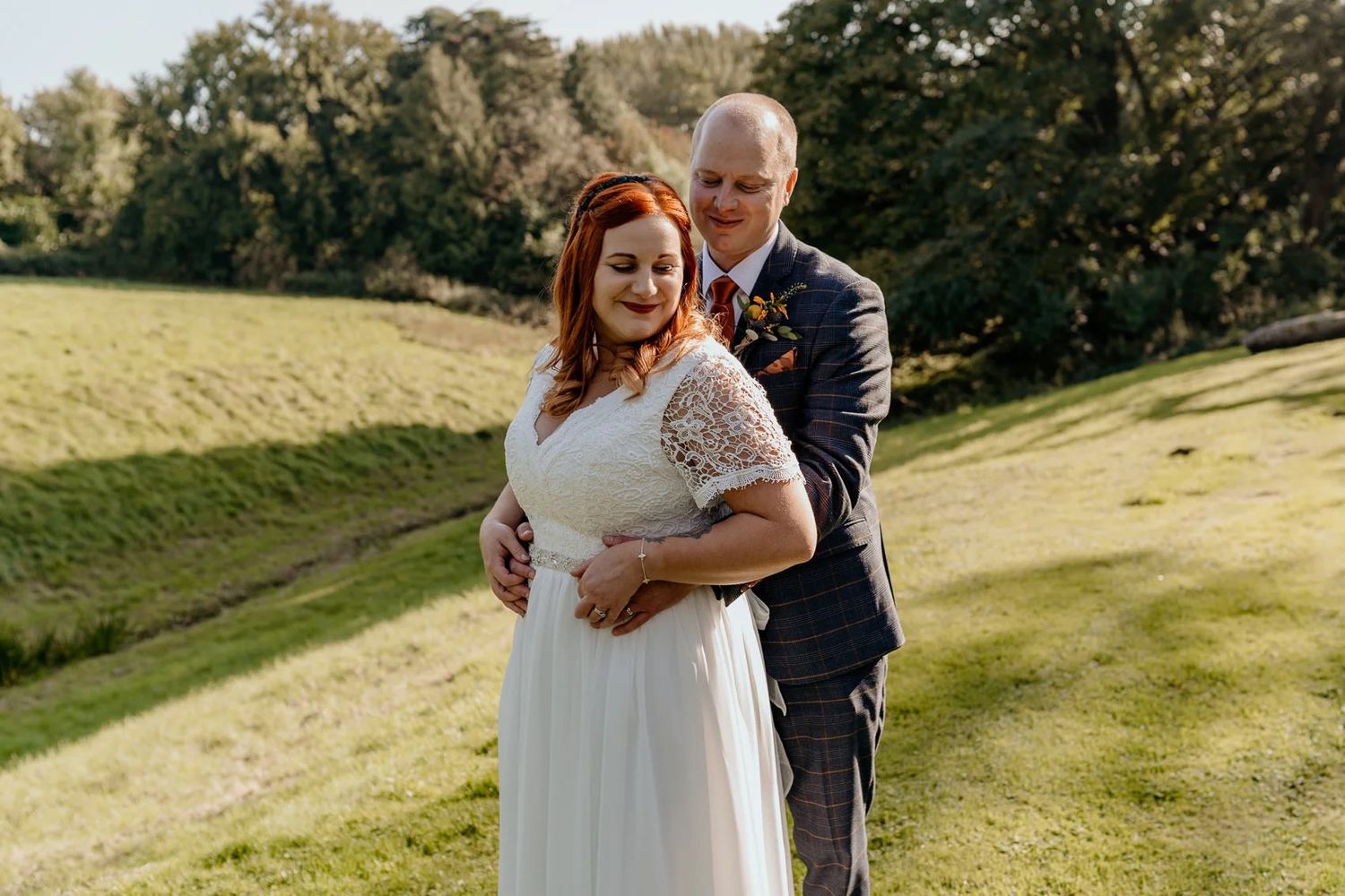Couple sharing intimate moment on grassy hillside during autumn wedding.