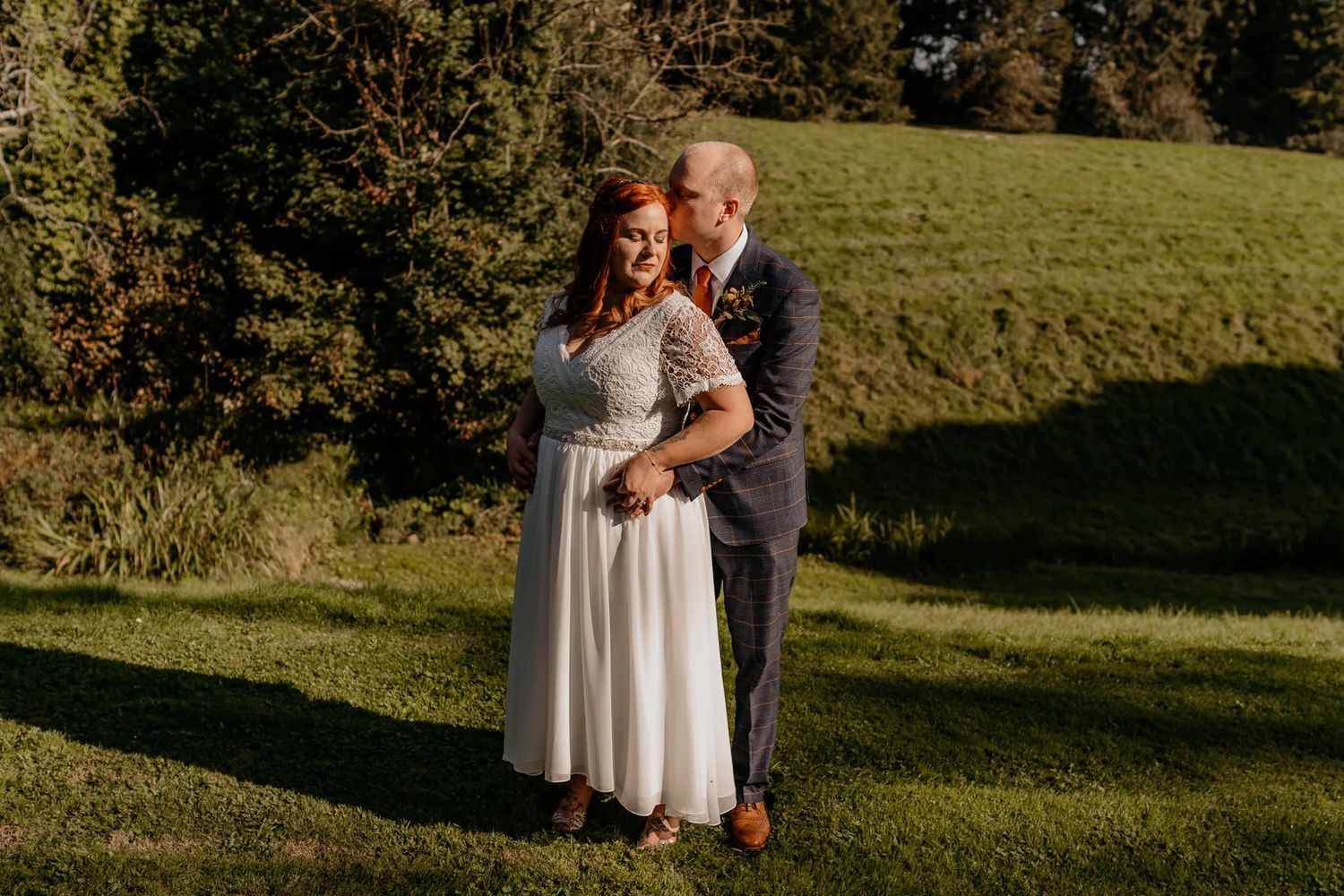 A couple shares an intimate moment together on a grassy hill during golden hour.