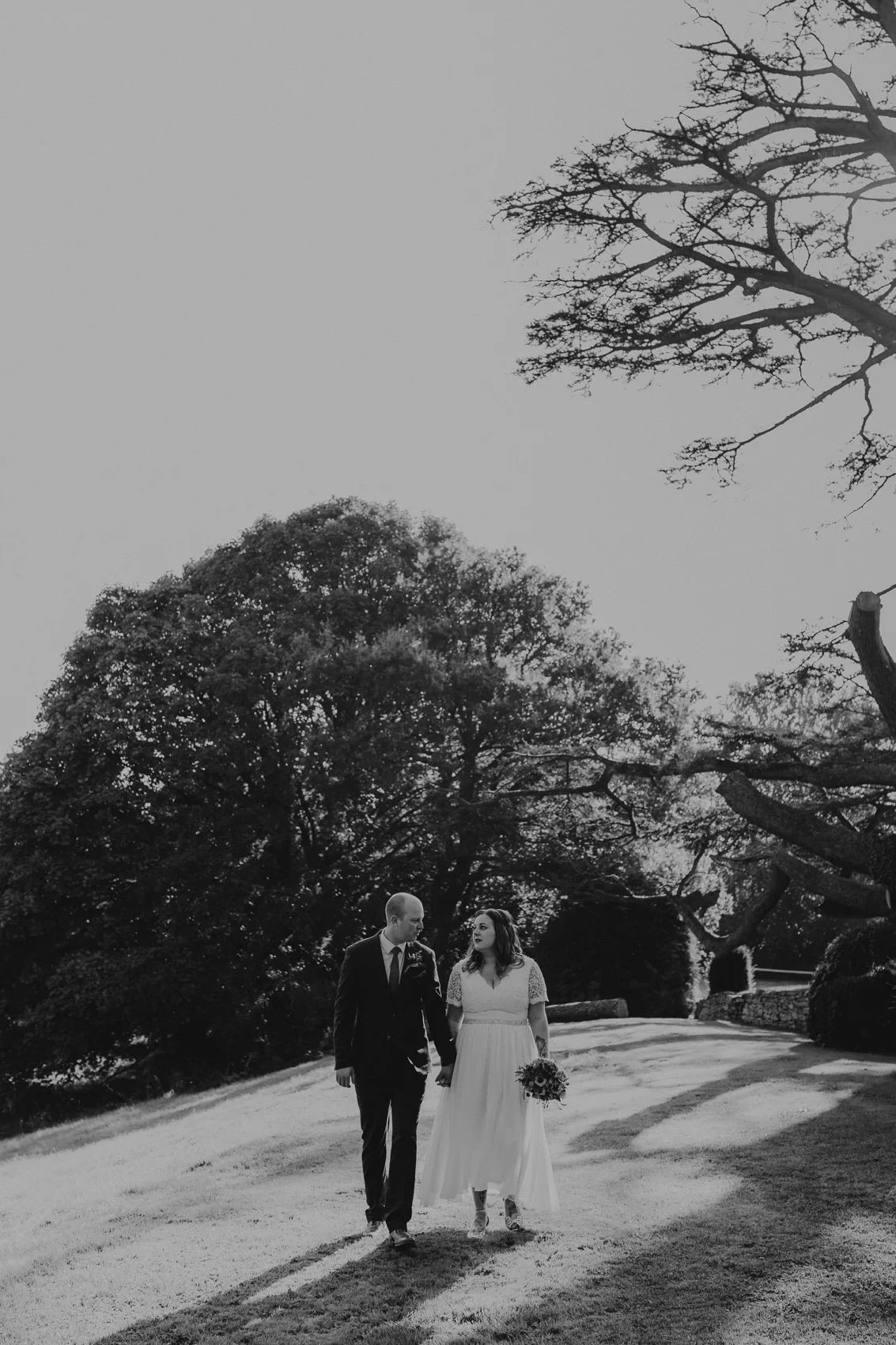 Black and white photograph of a couple walking on a hillside beneath bare trees.