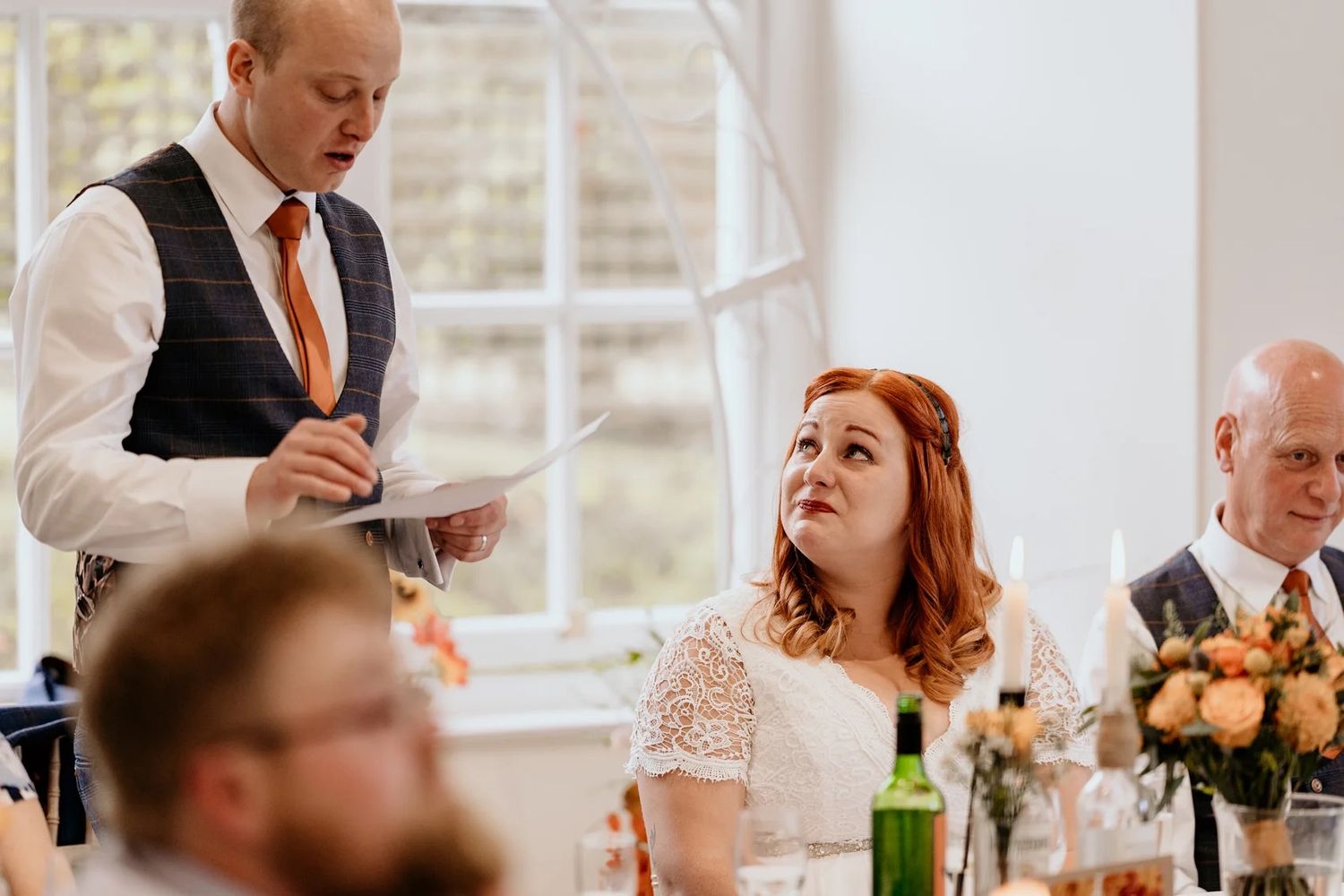 Wedding reception guests engage in conversation while seated at tables decorated with floral centerpieces.