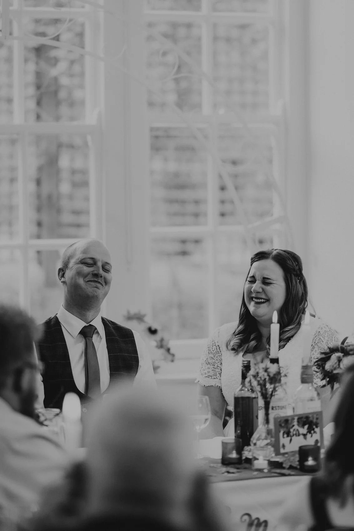 Wedding guests laughing and enjoying themselves at reception tables during formal dinner celebration.