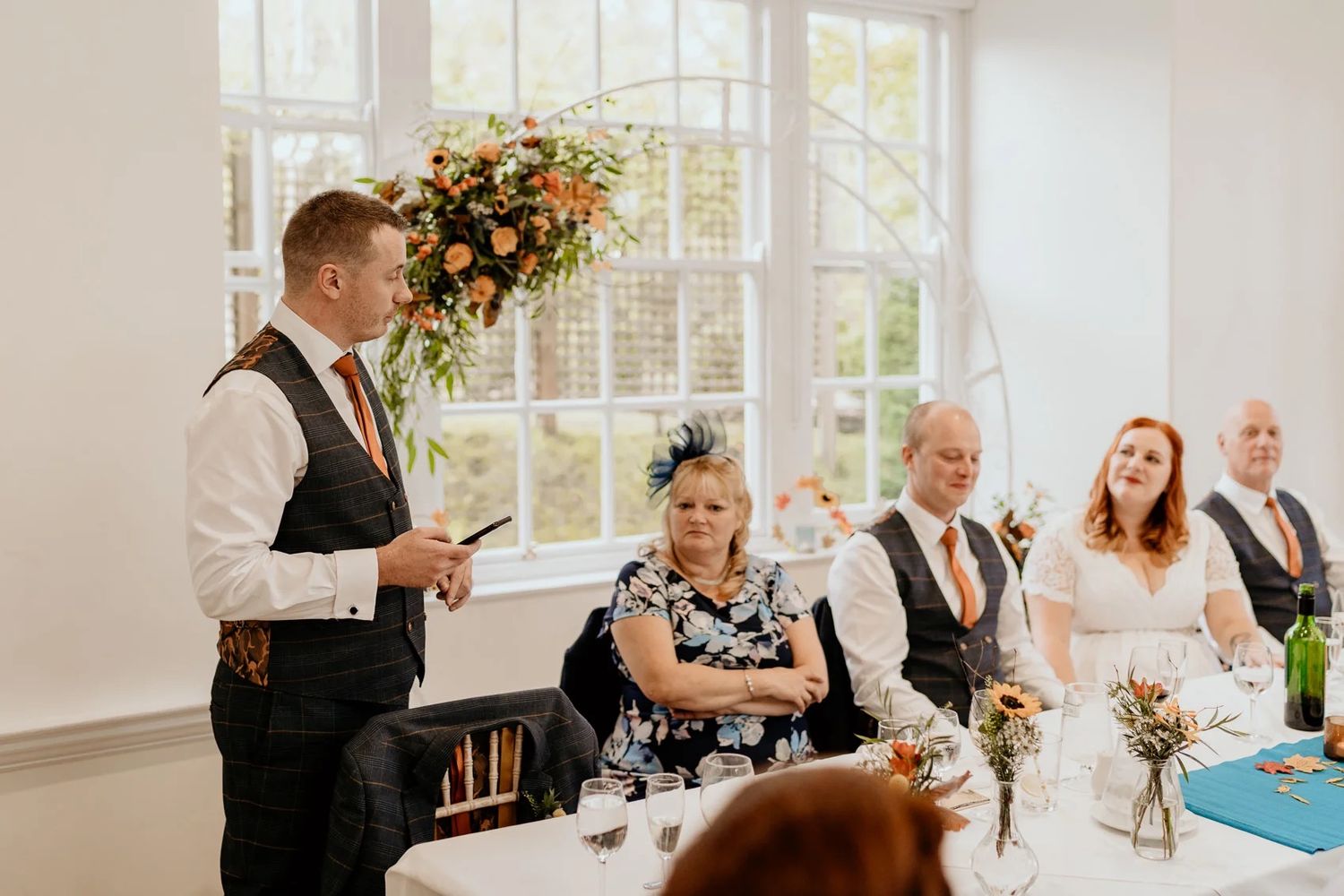 Wedding reception in bright sunlit venue with window views and floral decor.