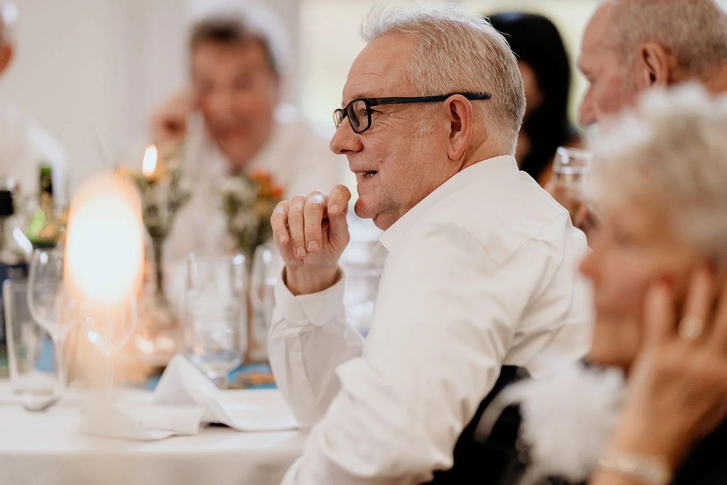 Wedding reception guests seated at elegant candlelit tables in a bright, festive dining room.