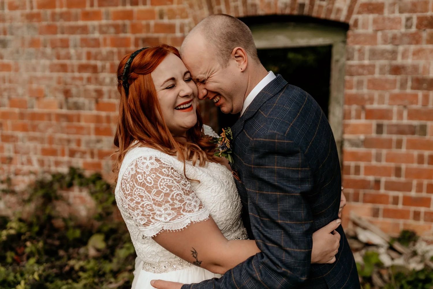 A romantic moment between a bride in lace and groom against rustic brick walls.