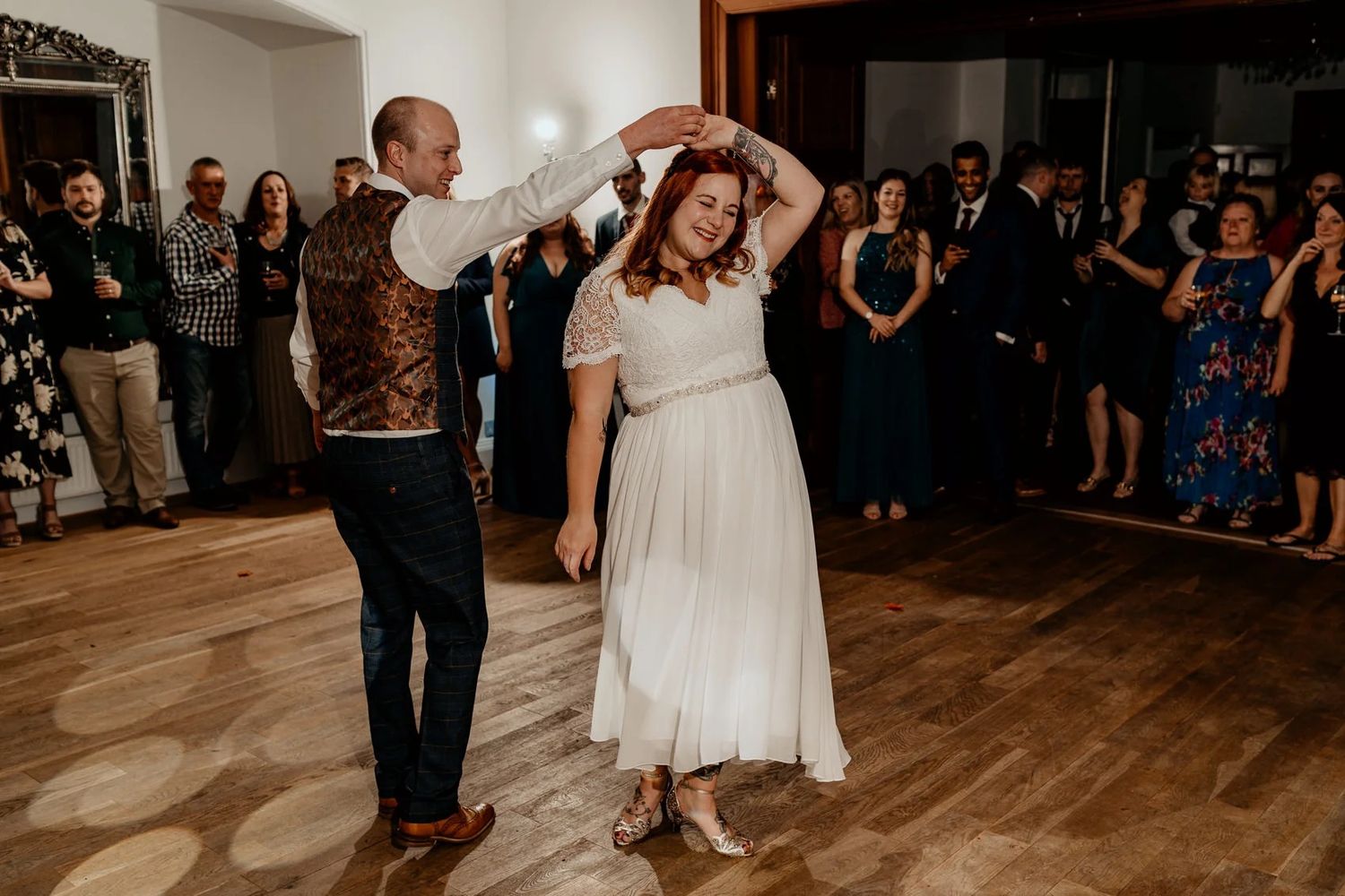 Wedding guests dancing and celebrating on a wooden dance floor at an evening reception.